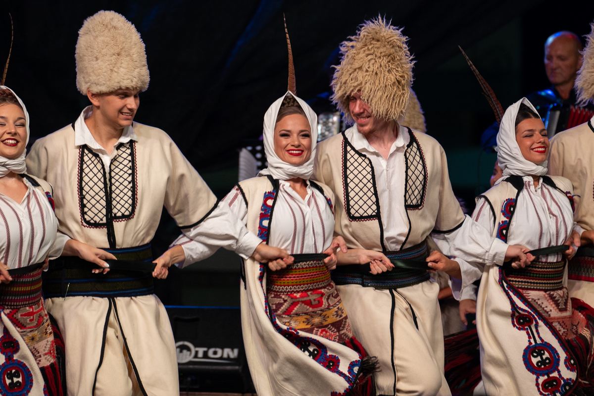 Igrači u belim nošnjama sa krznenim kapama i igračice u maramama u kolu